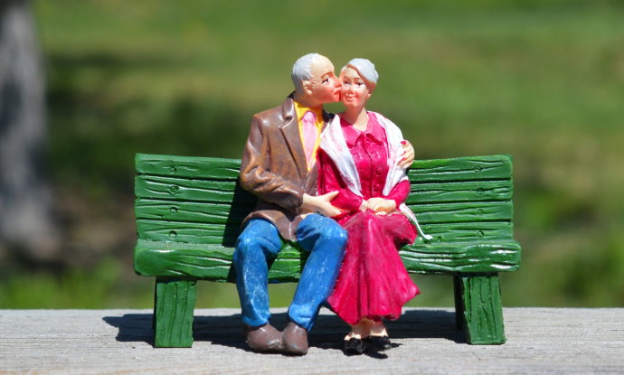 Boneco de casal de ideosos sentados em banco no parque.